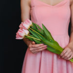Young woman wearing a pink dress holding a bouquet of pink flowers for valentines day.