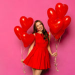 Young woman wearing a red dress and holding love heart balloons for valentines day.