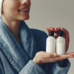 Woman wearing a robe and towel holding two bottles of beauty products. Image used for a 3D facial treatment blog.