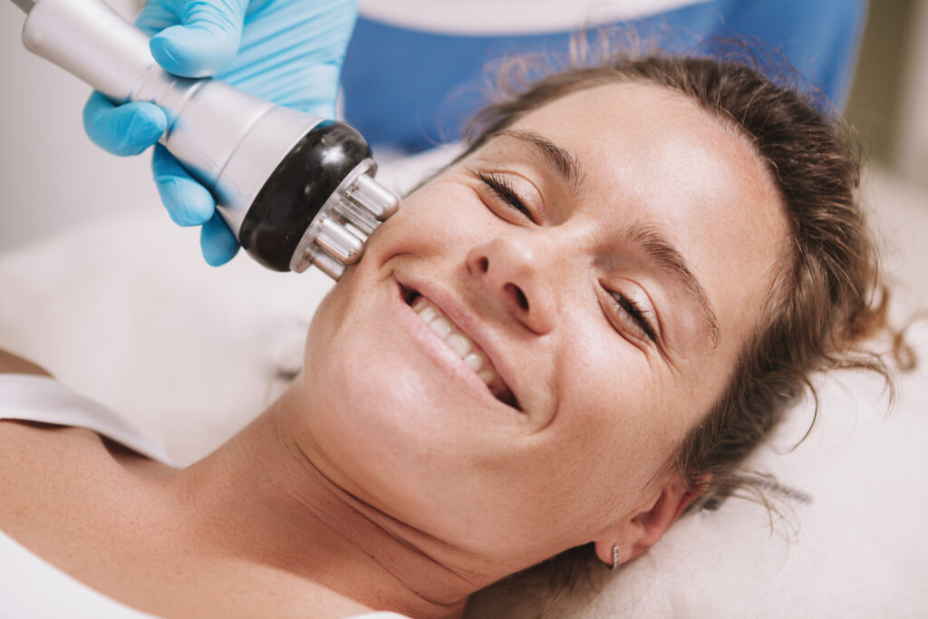 Close up shot of a happy mature woman smiling, enjoying rf-lifting facial treatment at beauty clinic. Happy healthy woman getting radio frequency skin tightening procedure by cosmetologist
