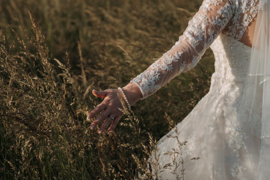The bride walking in a wheat field wearing a beautiful wedding dress and a pearl bracelet